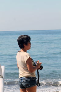 Side view of woman standing at beach holding a camera 