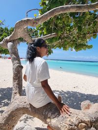 Woman sitting on beach by sea against sky