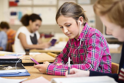 Schoolgirl listening music through smart phone in classroom