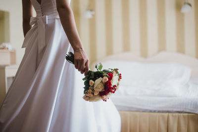 Midsection of bride holding bouquet at home