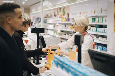 Pharmacists and customers standing at checkout in medical store