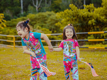 Cute sisters holding flag standing on grass at park