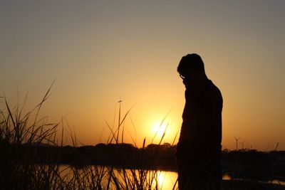 Silhouette woman standing by plants against sky during sunset