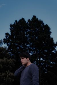 Young man looking away against trees