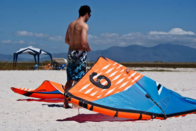 Full length of shirtless man standing at beach against sky