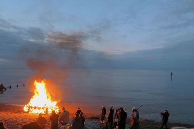 People by campfire at beach against sky