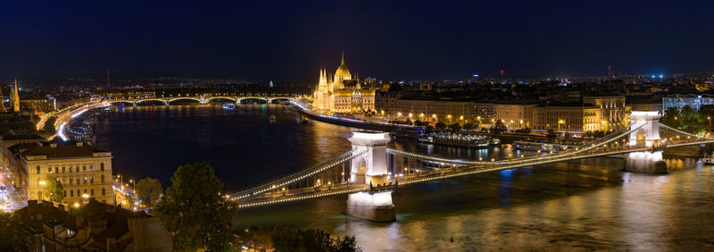 Illuminated bridge over river in city at night