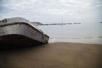 Abandoned boat moored on beach against sky