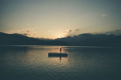 Silhouette person in lake against sky during sunset