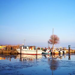 Boats moored at harbor against clear blue sky