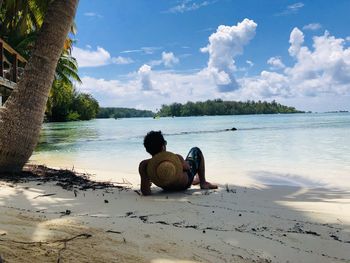 Rear view of woman sitting on beach against sky