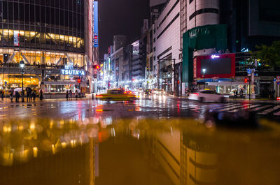 Illuminated city street by buildings at night