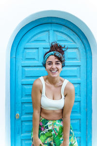 Portrait of smiling young woman standing against blue door