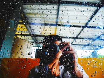 Man photographing seen through wet glass window