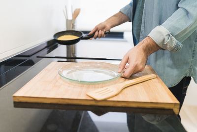 Man cooking in the kitchen in a denim shirt. an anonymous man is holding a pan with a pancake to put it on a plate