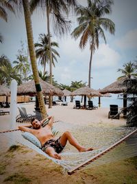 Full length of shirtless man relaxing in hammock on beach