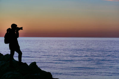 Man photographing sea against sky during sunset