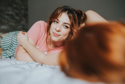 Crop young female girlfriends in pajamas relaxing on bed in bedroom