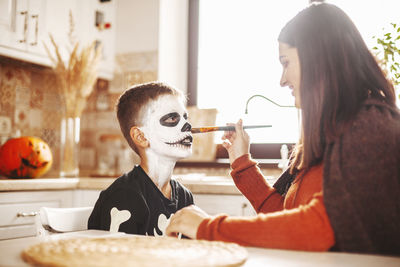 Close-up of smiling girl painting face of son at home