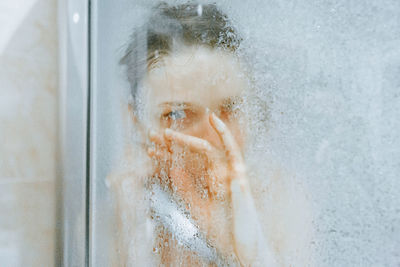 Close-up portrait of a serious young man looking through window