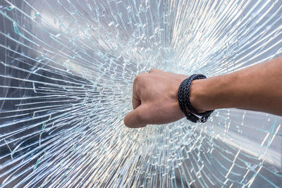 Cropped hand of man punching glass window