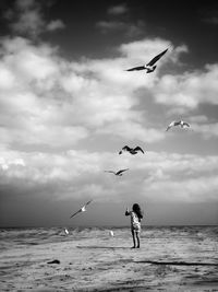 Girl standing with seagulls flying over beach against sky