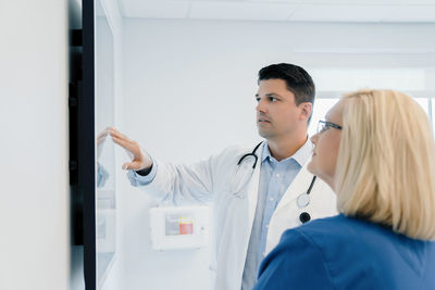 Doctor pointing at flat screen while discussing with female colleague in hospital