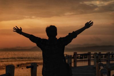 Rear view of man with arms outstretched standing on beach