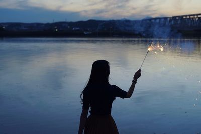 Silhouette of woman standing by lake holding sparkler