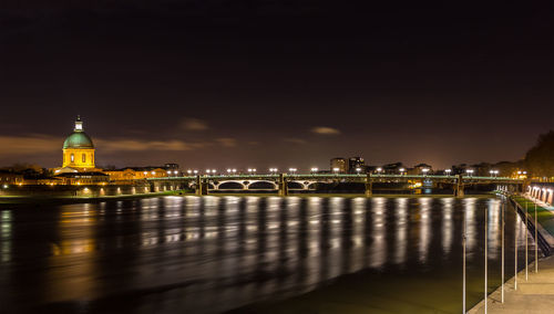 Illuminated bridge over river by buildings against sky at night