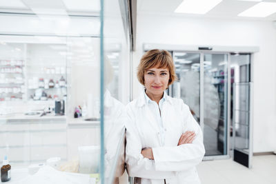 Smiling female professional with arms crossed leaning on glass wall