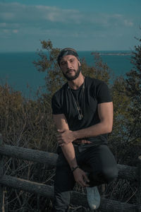 Young man looking away while sitting on land against sky