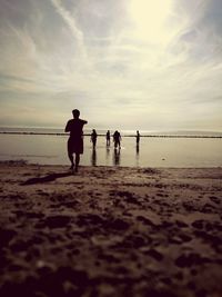 People at beach against sky during sunset