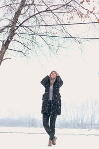 Full length portrait of woman standing on snow covered tree