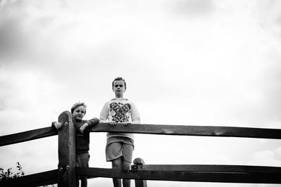 Low angle view of man sitting on railing against sky