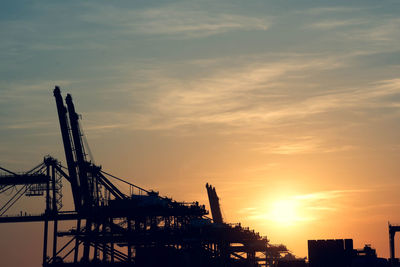 Silhouette cranes on pier against sky during sunset