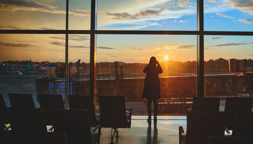 View on the aiport window with woman walking with suitcase at the departure hall during the sunset. 