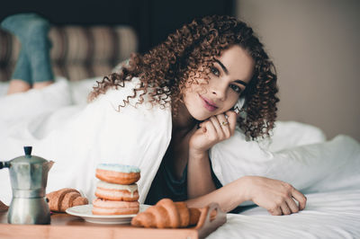 Portrait of woman lying by breakfast on bed at home