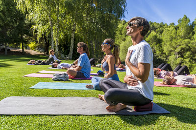 Mature male and female tourists practicing yoga on mat at health retreat during sunny day