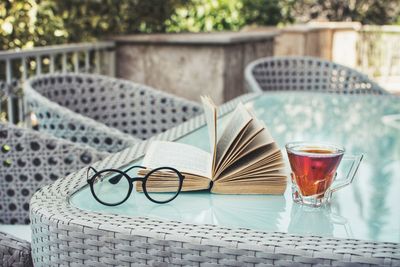 Close-up of glasses, an open book and a cup of tea on table