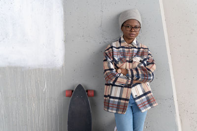 Portrait of woman with skateboard standing by wall