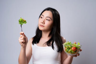 Portrait of woman holding ice cream against gray background