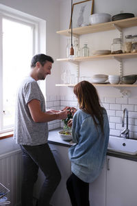 Couple preparing salad at kitchen counter by window