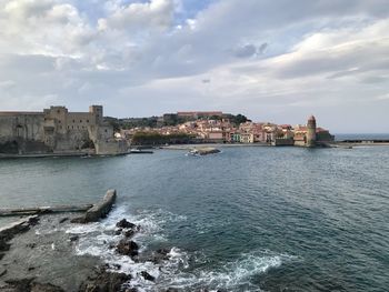 Buildings by sea against cloudy sky