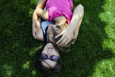 Overhead view of mother embracing daughter while lying on grassy field