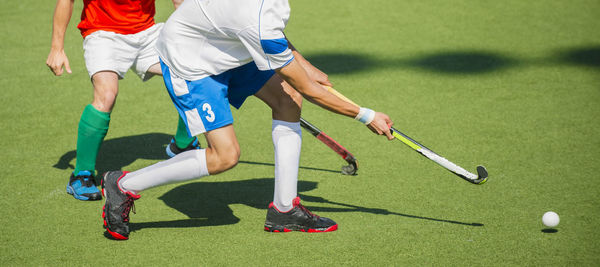 Low section of men playing hockey on turf