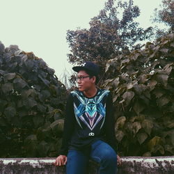 Young man sitting on tree against clear sky