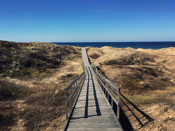 Boardwalk leading to sea against clear blue sky