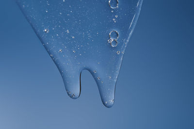 The texture of a gel or shampoo flowing down on a blue background.