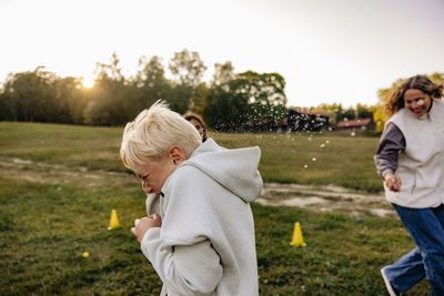 Side view of blond boy avoiding friends splashing water while playing in playground